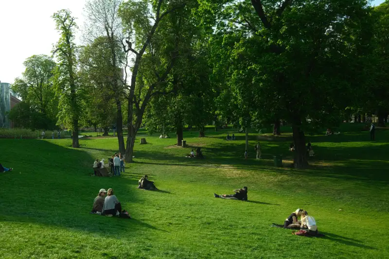 Pelouse d'un parc public arboré, des personnes assises à l'ombre des arbres