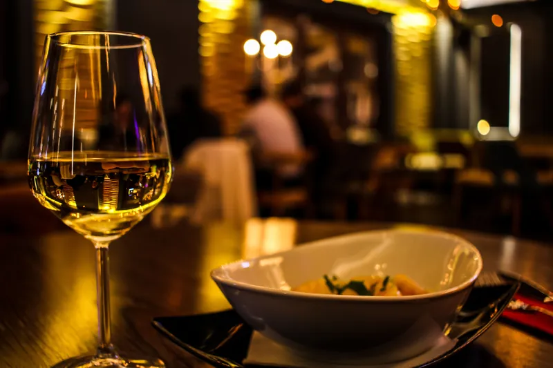 Verre de vin blanc et assiette servis sur une table de restaurant, salle à l'éclairage tamisé en arrière-plan